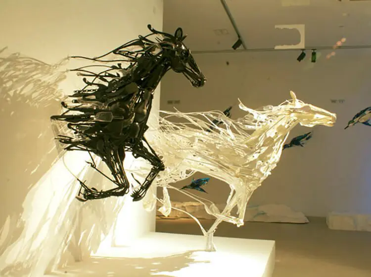 obra de sayanka ganz com dois cavalos, um preto e um branco, saindo de uma parede. ilustra a arte com reciclagerm