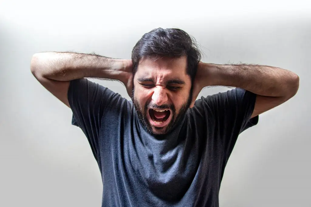 homem gritando, tapando as orelhas de olhos fechados, resposta comum aos estímulos da misocinesia